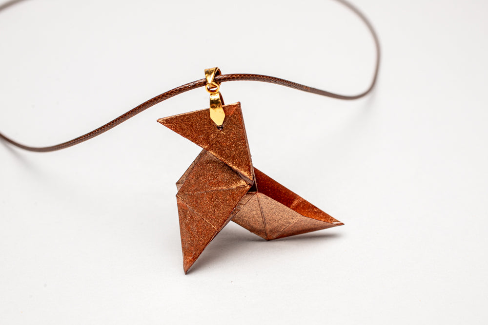 Colgante origami artesanal en papel cobre inspirado en La Casa de Papel sobre fondo blanco