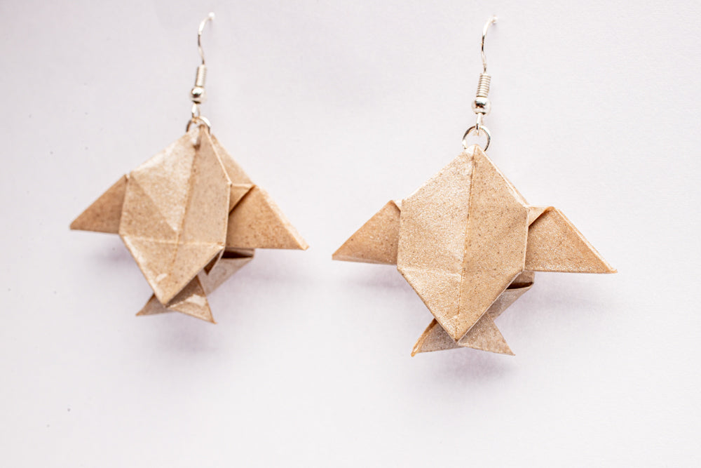 Aretes origami en forma de peces Luna beige con acabado tornasolado sobre fondo blanco