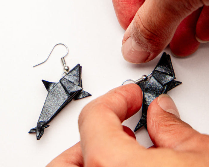 Manos y aretes de origami en forma de tiburón hecho en papel azul con resina